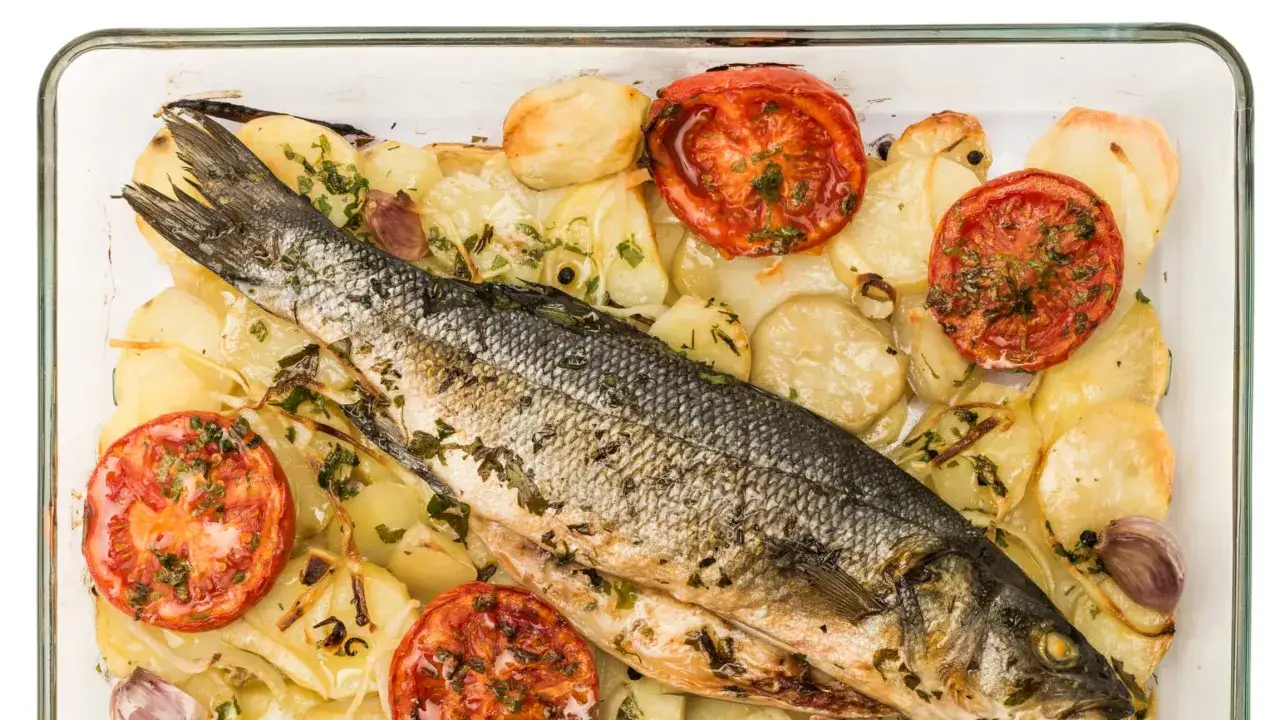 Un profumato branzino al forno con patate, pomodori e aglio, pronto per essere gustato.