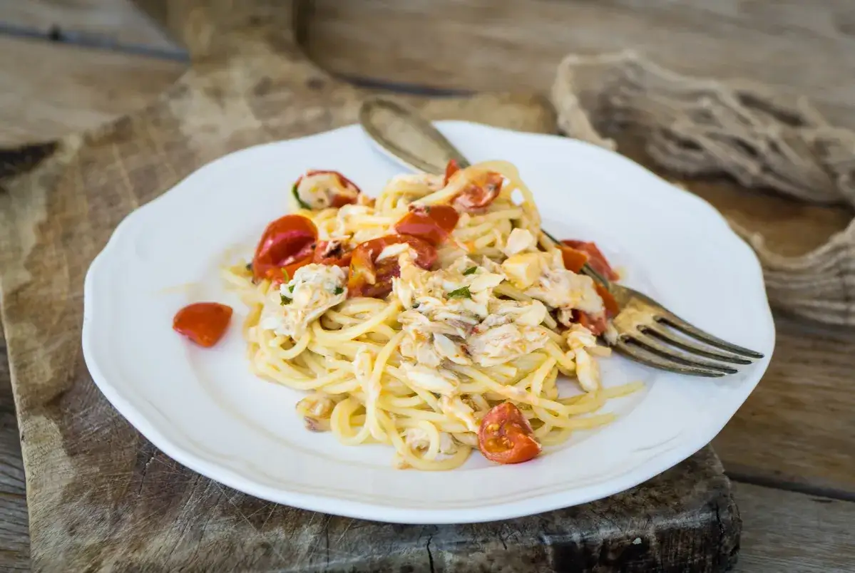 Spaghetti con sugo di pesce fresco, pomodorini e pezzi di granchio, serviti su un piatto bianco con forchetta.