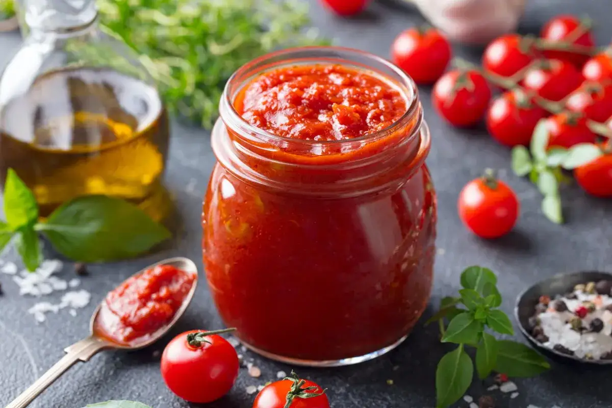 Un vasetto pieno di salsa di pomodoro fatta in casa da conservare, con pomodorini freschi, basilico e olio d'oliva.