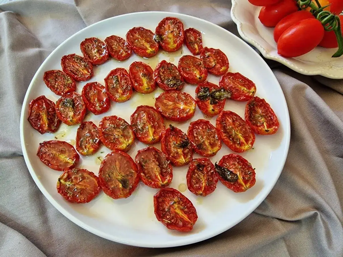 Pomodorini al forno, dorati e succosi, conditi con erbe aromatiche su un piatto bianco.