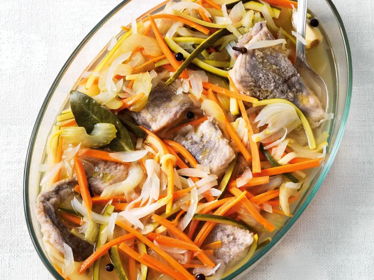Carpione piemontese in un piatto di vetro, con pesce, carote, zucchine, cipolle, sedano e spezie.