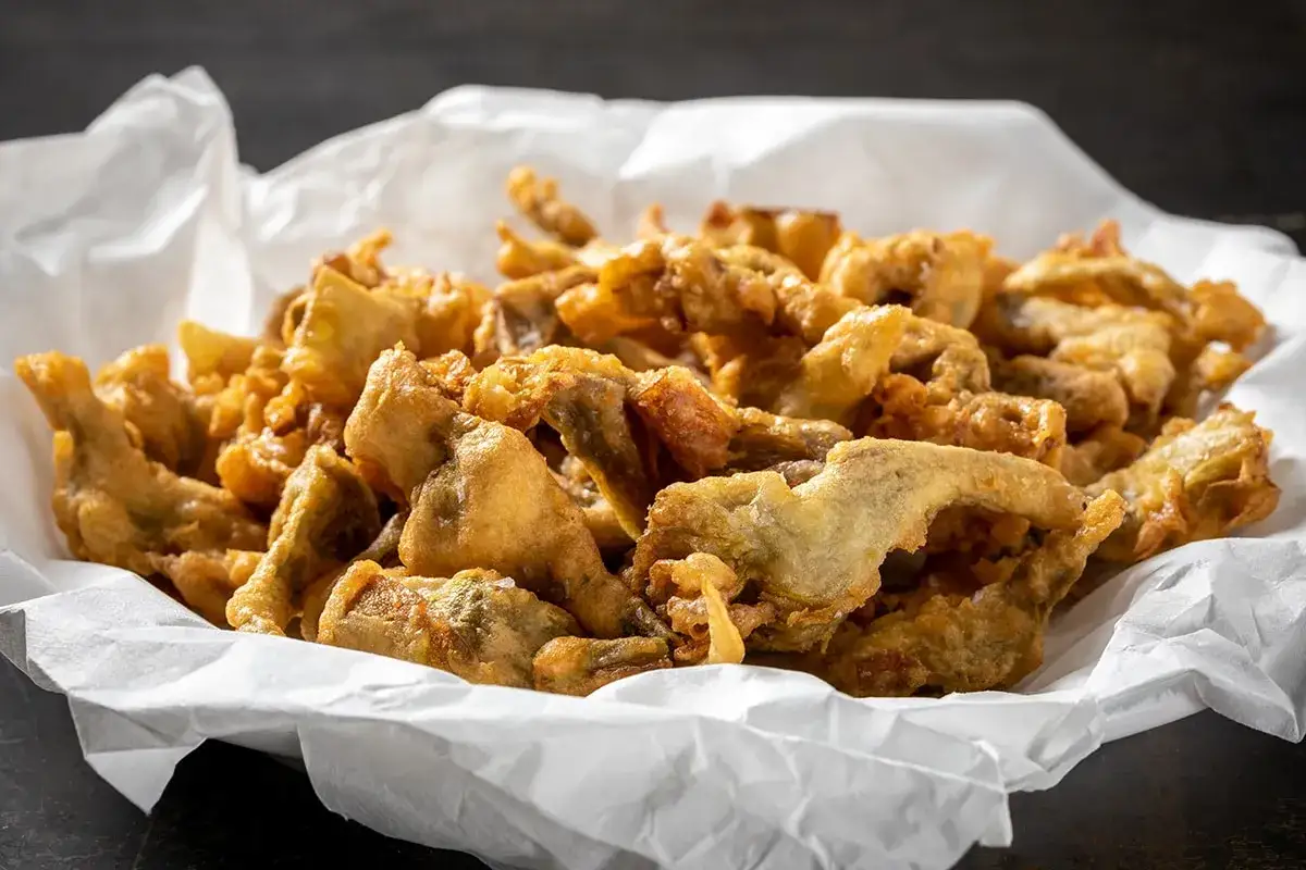 Un cestino di carta bianco pieno di croccanti carciofi fritti senza pastella, dorati e invitanti.