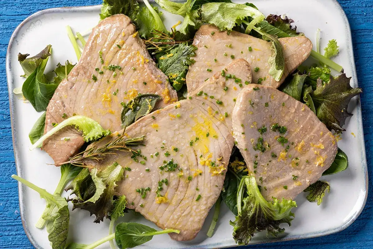 Fette di tonnetto al forno, condite con scorza di limone e erbe aromatiche, servite su un letto di insalata fresca.