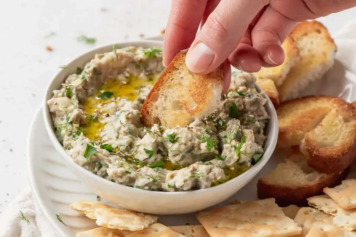 Un crostino di pane tostato affonda nel hummus di fagioli, guarnito con erbe fresche e olio d'oliva.