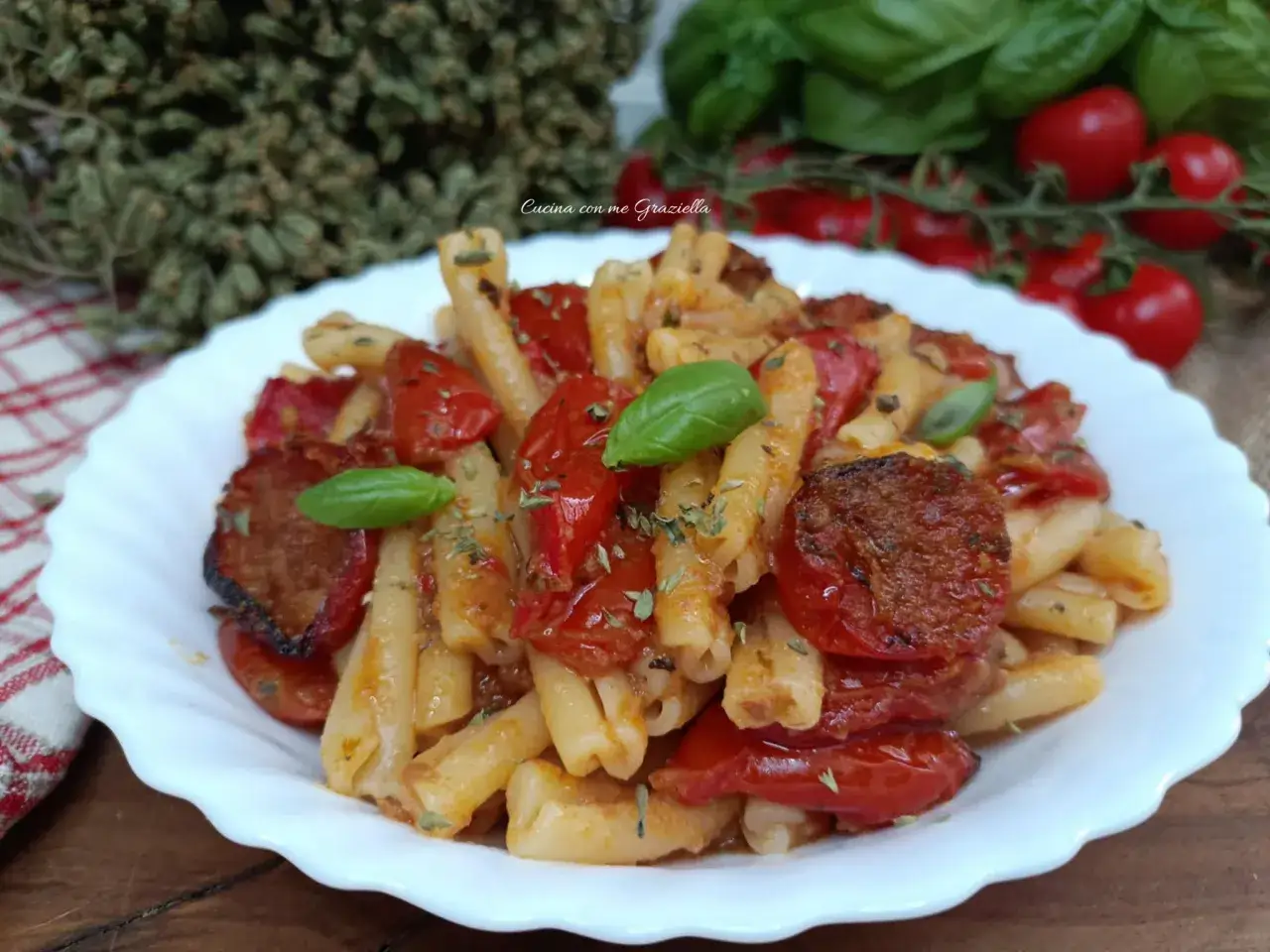 Piatto invitante di pasta con pomodori al forno alla pugliese, condita con erbe aromatiche e basilico fresco.