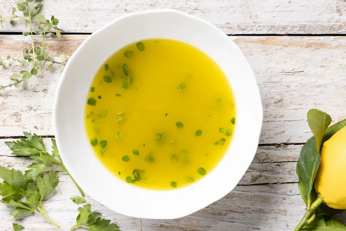 Una ciotola bianca contiene una vibrante salsa vierge, guarnita con erbe fresche e un limone accanto.