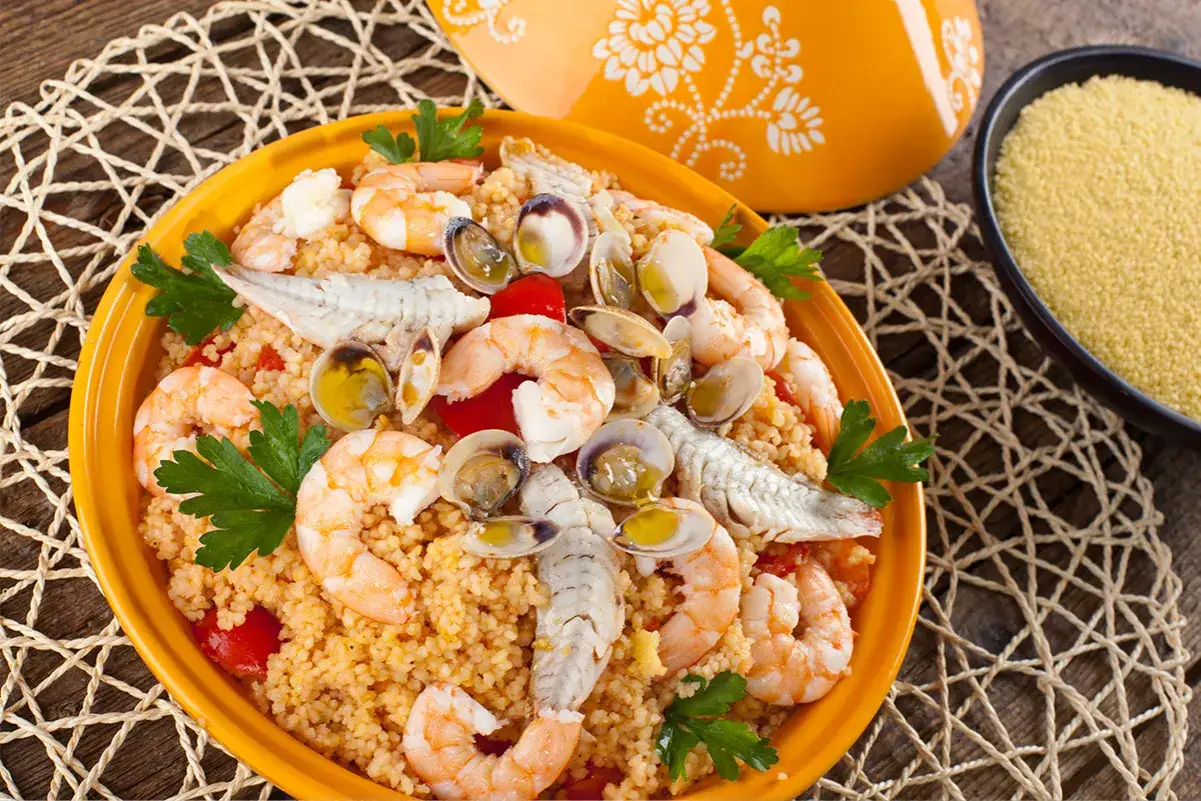 Piatto di cous cous con gamberi, vongole e pesce, un'idea per come condire il cous cous in modo gustoso e colorato.