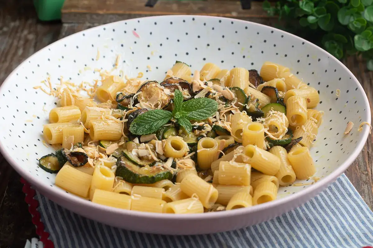 Piatto di pasta e zucchine alla siciliana, guarnito con menta fresca e scaglie di mandorle tostate.
