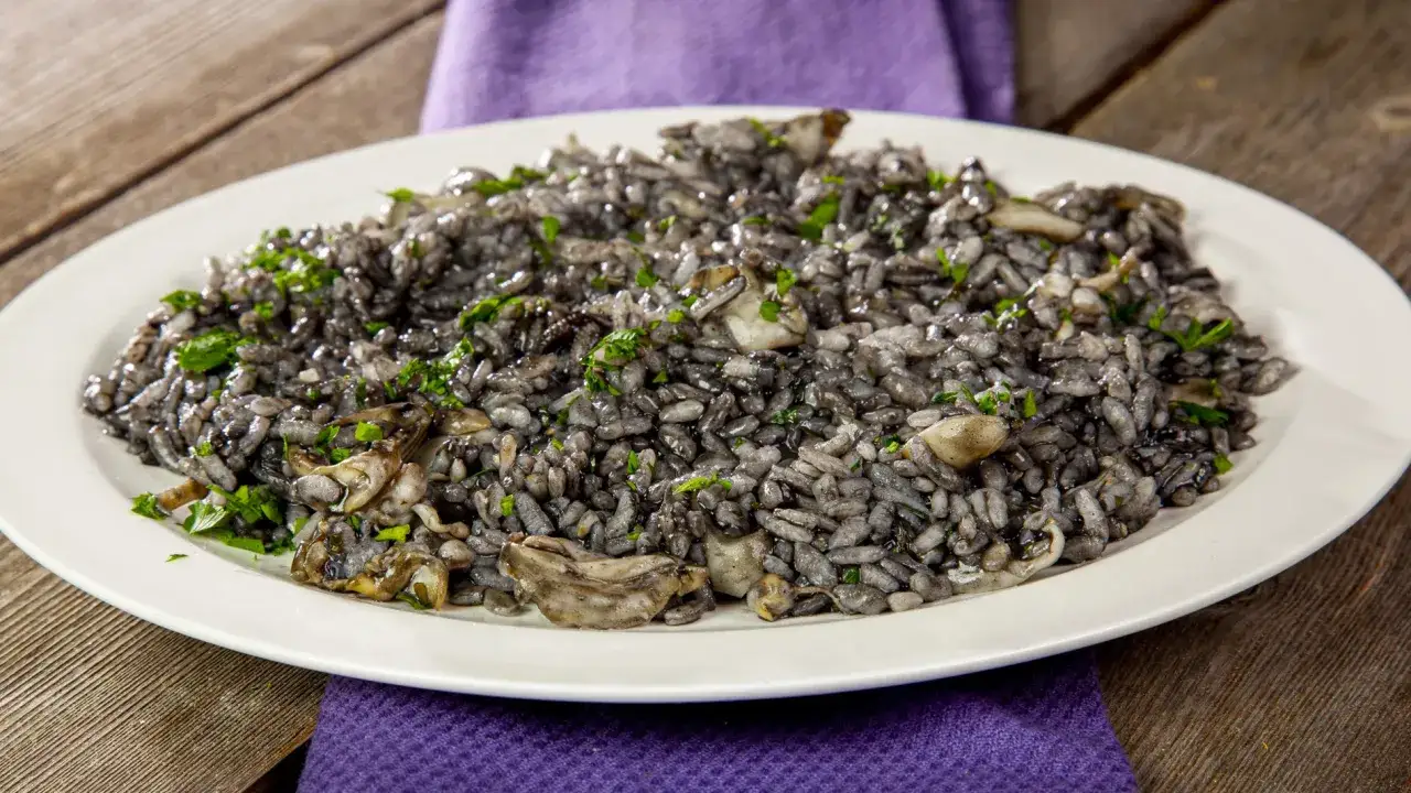 Piatto di risotto al nero di seppia, ricco e saporito, guarnito con prezzemolo fresco su un piatto bianco.