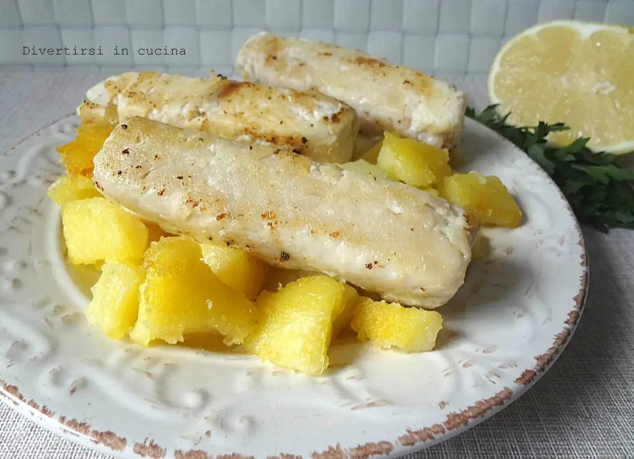 Delizioso merluzzo al limone con patate croccanti, guarnito con prezzemolo e una fetta di limone.