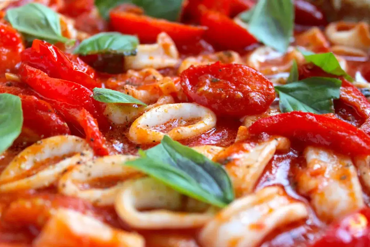 Un gustoso sugo freddo per pasta con calamari, pomodorini e basilico fresco, pronto per essere gustato in una calda giornata estiva.