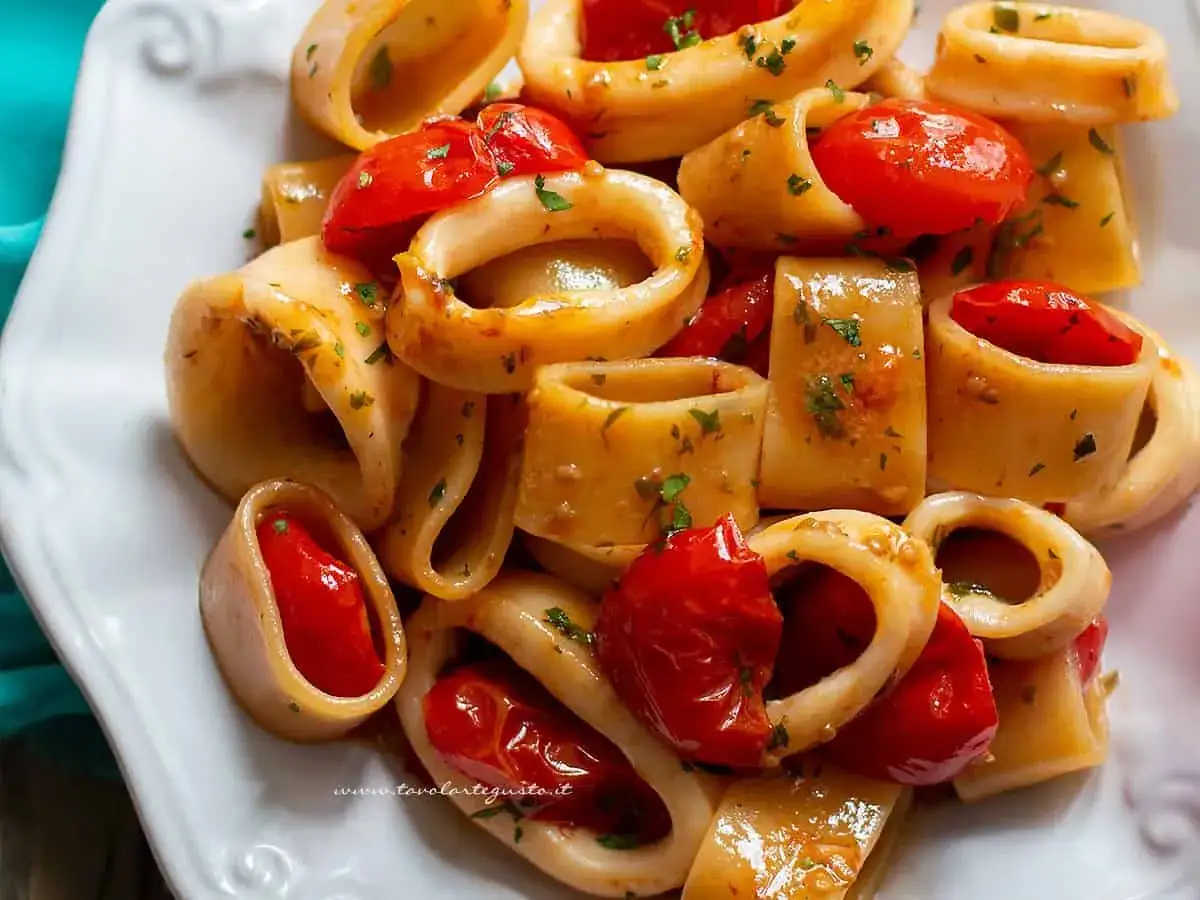 Piatto di calamarata ricetta originale con calamari e pomodorini freschi, condita con erbe aromatiche.