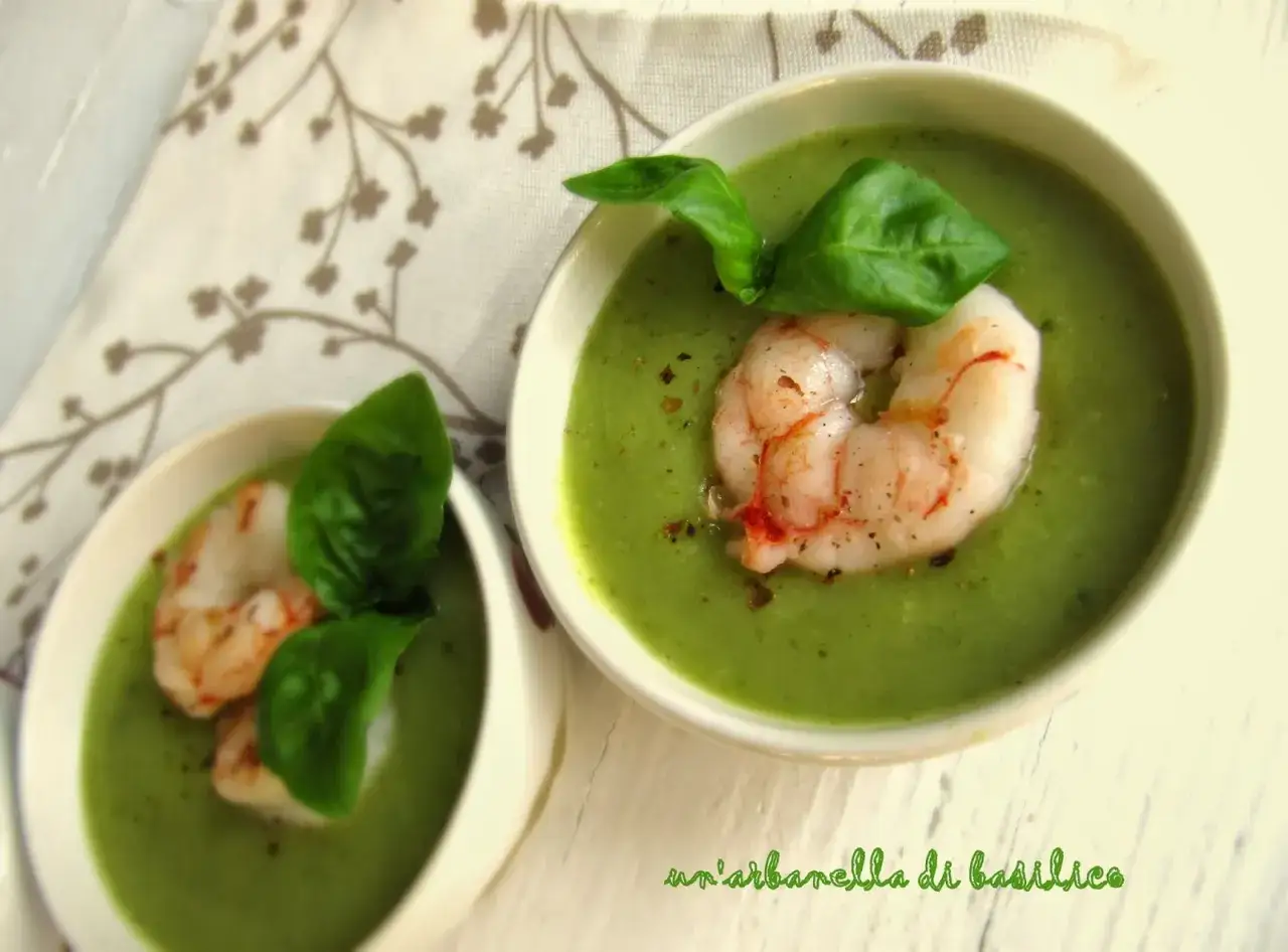 Vellutata di zucchine cremosa con gamberi e basilico fresco, servita in ciotole bianche su un tovagliolo decorato.