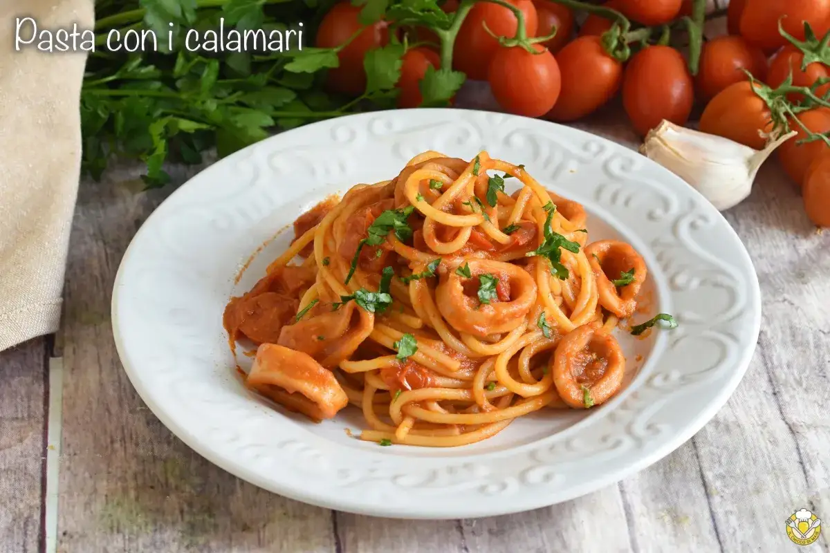 Spaghetti con calamaretti in salsa rossa, guarniti con prezzemolo fresco. Sullo sfondo pomodorini e aglio.
