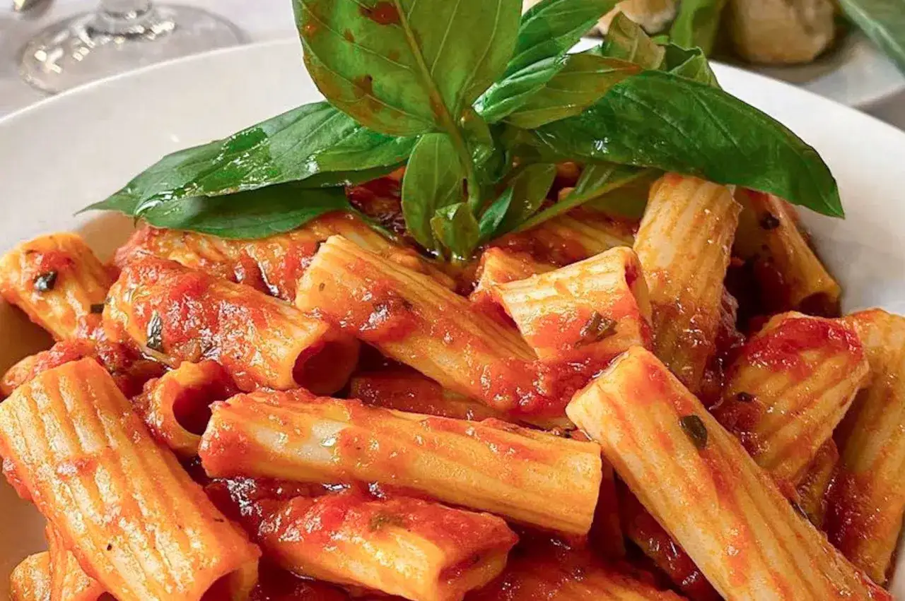 Rigatoni al sugo, un classico dei primi piatti pasquali, guarniti con foglie di basilico fresco.