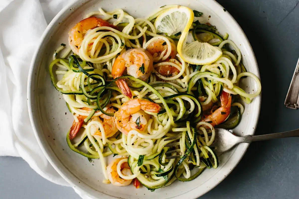 Un piatto di spaghetti di zucchine con gamberi succulenti e spicchi di limone, un'esplosione di freschezza e sapore.