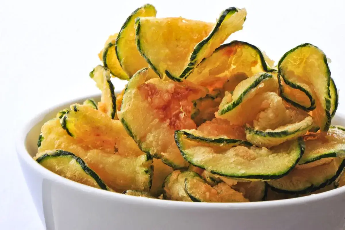 Fette croccanti di zucchine in pastella dorata, servite in una ciotola bianca.