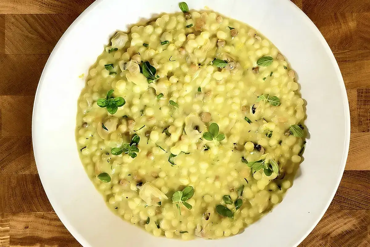 Piatto di fregola con vongole, arricchito da erbe fresche e un tocco di limone. Un classico sapore di mare.
