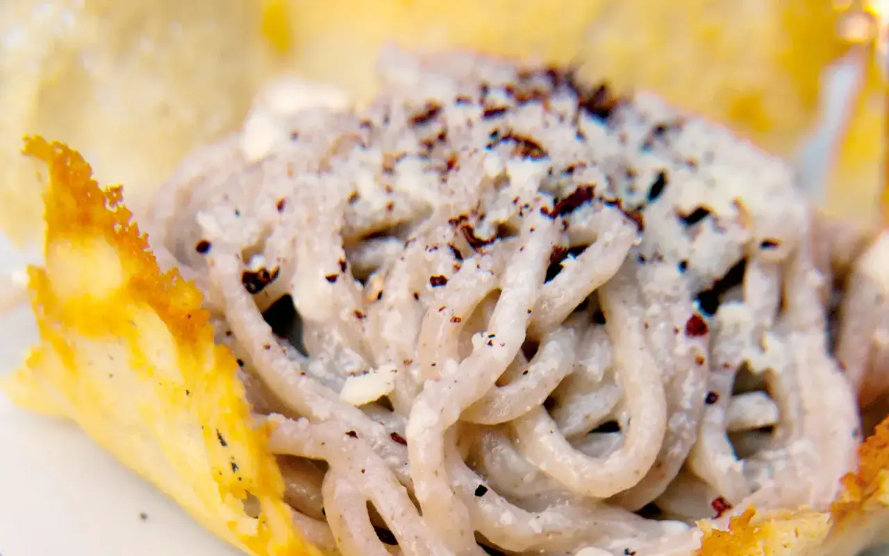 Un piatto di tonnarelli pasta cremosa, conditi con pepe nero e serviti in un cestino croccante di parmigiano.