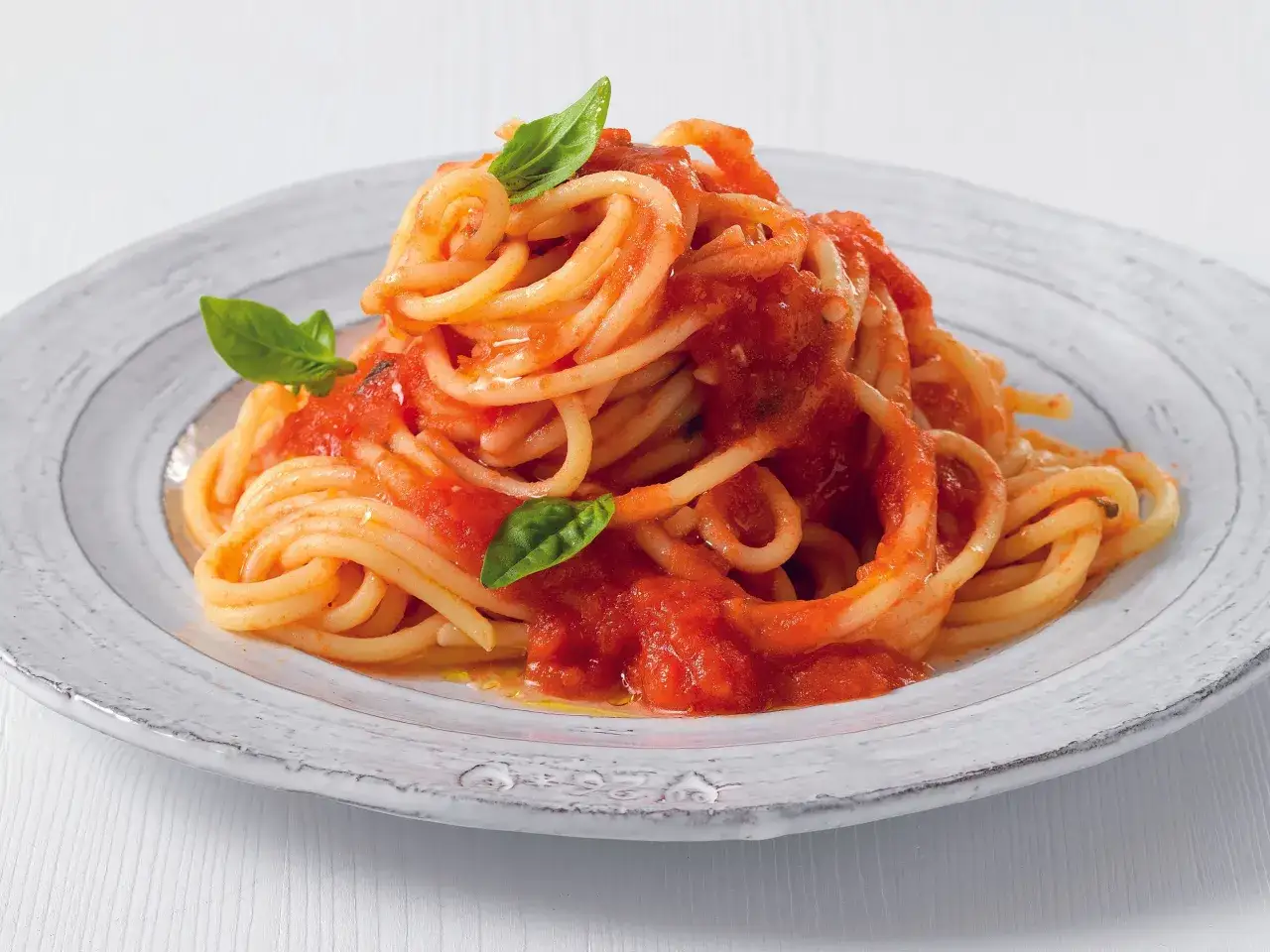 Un piatto di pasta al pomodoro fumante, condita con un sugo rosso vivo e guarnita con foglie di basilico fresco.