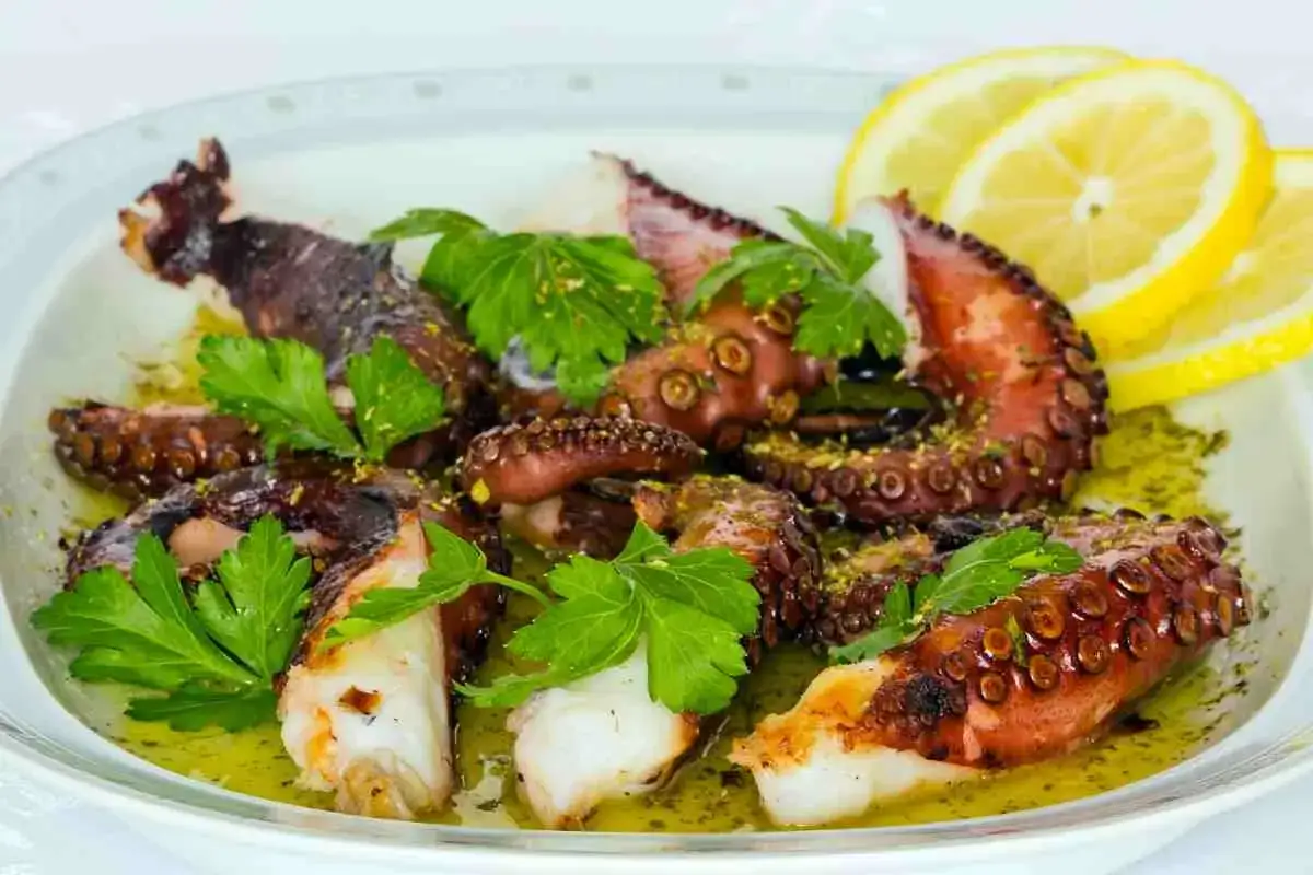 Tentacoli di polpo alla griglia, succulenti e profumati, serviti con prezzemolo fresco e spicchi di limone.