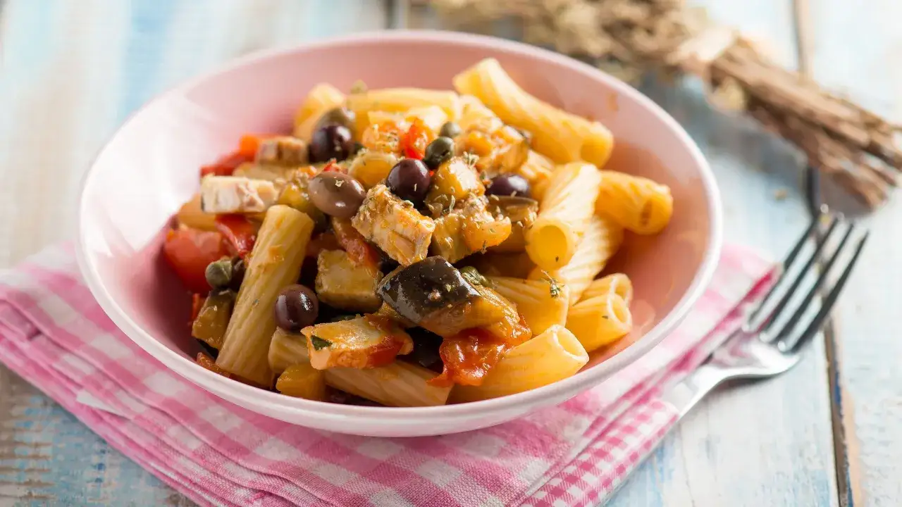 Piatto di pasta con pesce spada, melanzane, pomodorini e olive nere, condito con erbe aromatiche.