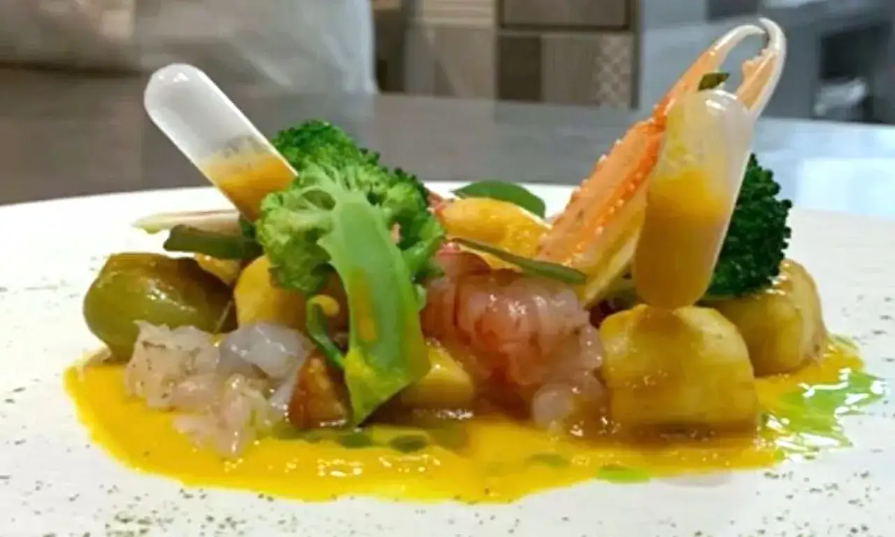 Gnocchi alla busara con gamberi, scampi e broccolo, serviti con una salsa gialla in provette.