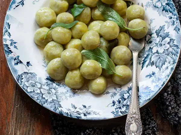 Piatto di gnocchi di zucchine fatti in casa, conditi con burro e salvia, su un piatto decorato con fiori blu.