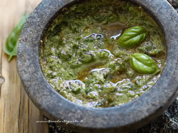 Mortai con pestello pieno di profumato pesto alla genovese, guarnito con foglie di basilico fresco.