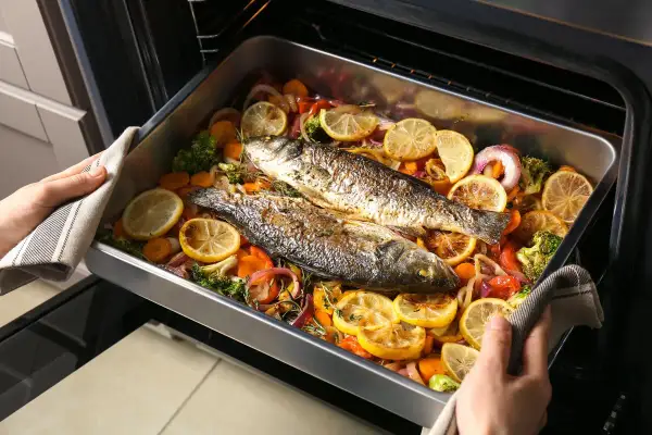 Due pesci interi, pronti per essere serviti, adagiati su un letto di verdure colorate e limone in una teglia. Un delizioso tonnetto al forno in preparazione.