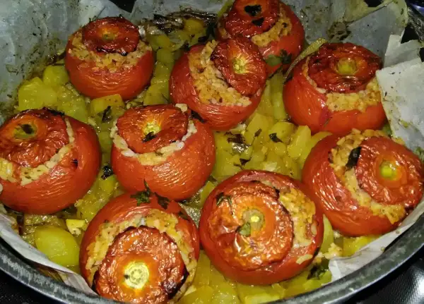 Pomodori ripieni di riso, cotti al forno su un letto di patate e erbe aromatiche. Un piatto saporito e colorato.