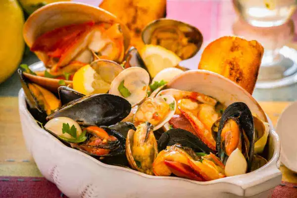 Un invitante piatto di zuppa di crostacei, ricco di cozze, vongole e gamberi, guarnito con limone e pane tostato.