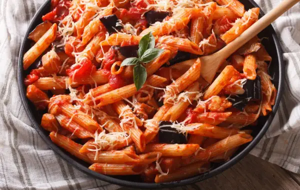 Piatto invitante di pasta con melanzane e pomodorini, condita con formaggio grattugiato e basilico fresco.