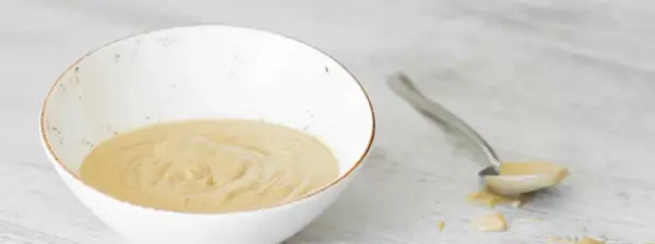 Una ciotola bianca contiene una cremosa salsa tonnata, con un cucchiaio che ne raccoglie una porzione.