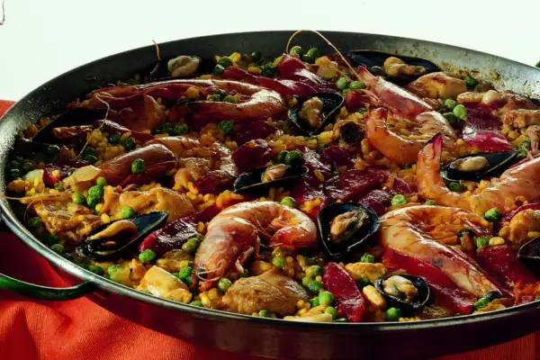 Un'abbondante paella valenciana in una padella, ricca di gamberi, cozze, piselli e pezzi di carne.
