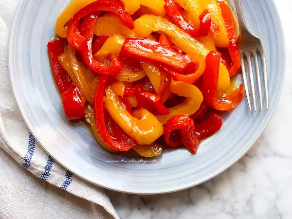 Peperoni in agrodolce, un contorno colorato e saporito, servito su un piatto azzurro con forchetta.