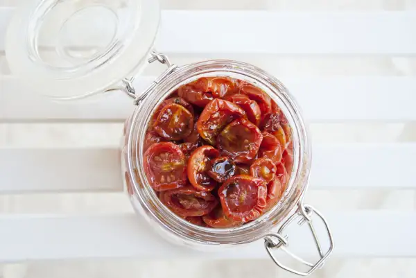 Barattolo di vetro pieno di succulenti pomodorini confit, pronti per insaporire ogni piatto.