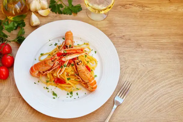 Un piatto di linguine con scampi, pomodorini e prezzemolo, uno dei migliori primi di pesce, pronto per essere gustato con un bicchiere di vino bianco.