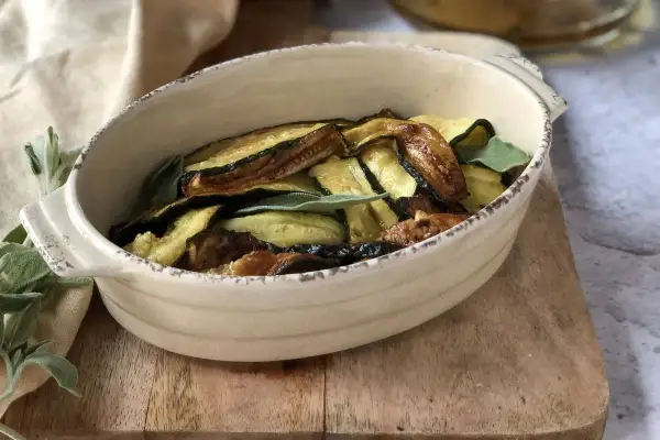 Zucchine in carpione dorate e saporite, guarnite con foglie di salvia fresca, servite in una ciotola di ceramica.