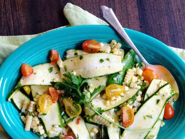 Insalata estiva con zucchine crude a fette, mais e pomodorini ciliegino, guarnita con prezzemolo fresco.