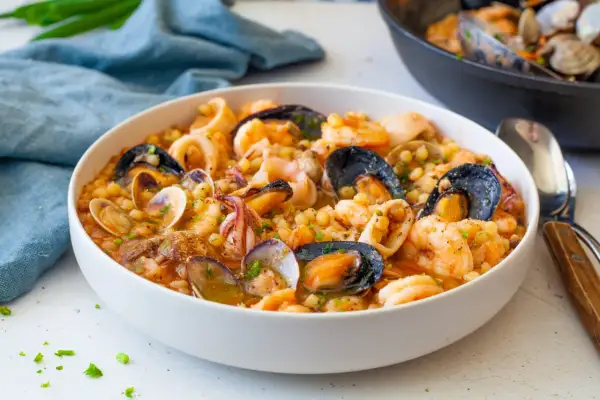 Un invitante piatto di fregola sarda con frutti di mare freschi: cozze, vongole, gamberi e calamari, condito con erbe aromatiche.