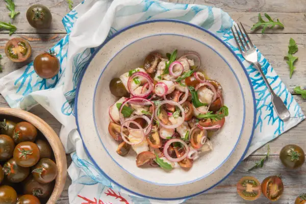 Rana pescatrice alla catalana: un'insalata fresca con pomodorini scuri, cipolla rossa e pesce bianco.