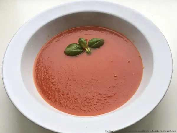 Una ciotola bianca contiene una vellutata salsa di pomodoro classica, guarnita con foglie di basilico fresco.