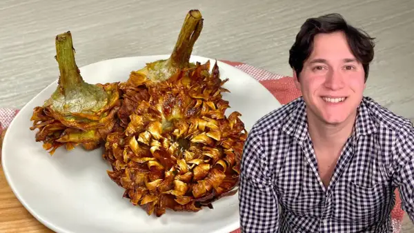 Due carciofi alla giudia dorati e croccanti su un piatto bianco, accanto a un uomo sorridente.