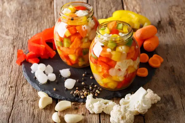 Due barattoli di giardiniera fatta in casa, pieni di verdure colorate come peperoni, carote e cavolfiore, pronti per essere gustati.