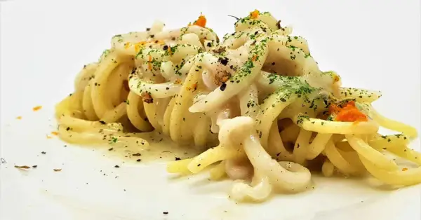 Un piatto di tonnarelli pasta conditi con una cremosa salsa bianca, guarniti con prezzemolo tritato e scorza d'arancia.