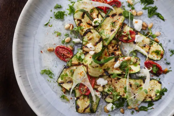 Zucchine grigliate come condirle: un piatto fresco con pomodorini secchi, pinoli, feta e erbe aromatiche.
