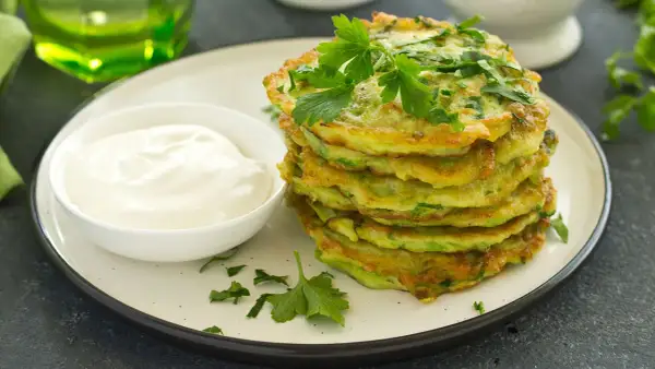 Frittelle dorate di zucchine trombetta, guarnite con prezzemolo fresco, servite con una ciotola di panna acida.