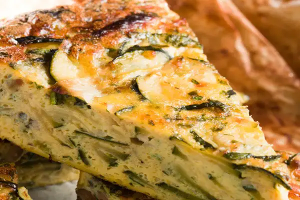 Fetta di torta salata con pasta sfoglia e zucchine, dorata e invitante, con verdure ben visibili nell'impasto.