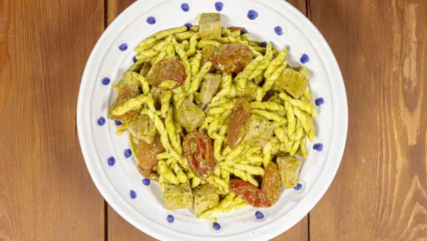 Un piatto di pasta alla carlofortina con trofie condite con pesto, pomodorini secchi e cubetti di tonno.